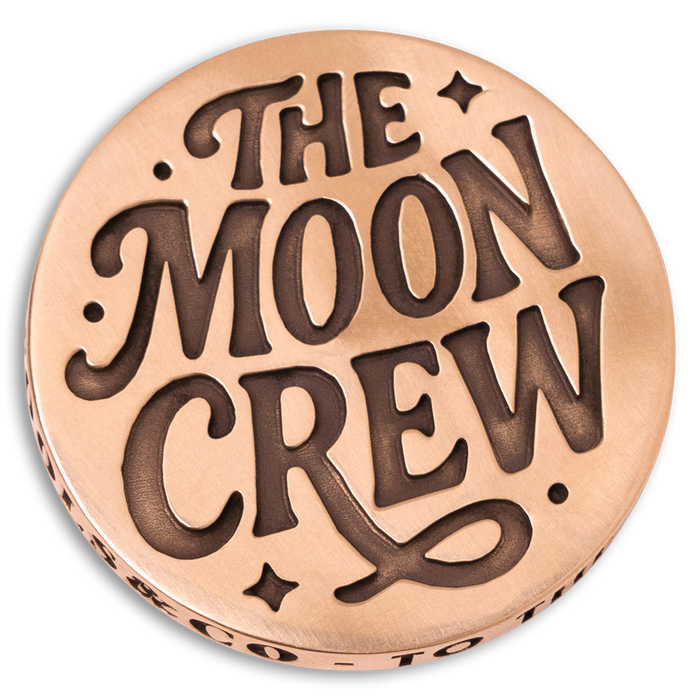 A round copper-colored metal coin or medallion engraved with the words 'THE MOON CREW' in dark brown lettering, shown on a plain white background.