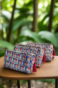 Two floral-patterned pouches with tassels on a wooden surface, blurred green foliage in the background